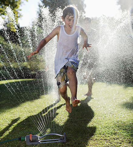 Young child laughing as they run through jets of water spraying up from a lawn sprinkler.