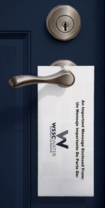 WSSC Water door hanger, hanging from a silver doorknob. A silver lock is above the knob. The door is dark blue with panels. 