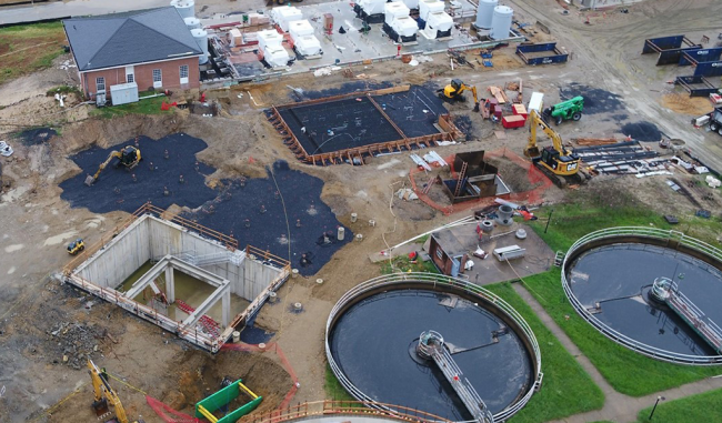 The Cake Receiving pit is in the middle of this photo with the concrete walls and two dark areas above it are stone blankets being prepared for concrete slabs.  There are a couple dozen piles poking up out of the ground on the slabs.  These piles will support 2 large silos that will store the sludge cake as it waits for processing.  To the right of the silos is another stone area being prepared for the Cambi Thermal Hydrolysis Processing equipment.