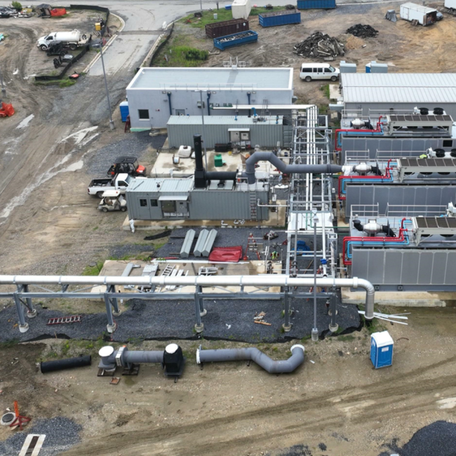 Workers are constructing the aerial pipe connection between the engine and the boiler in the middle of the photo.
