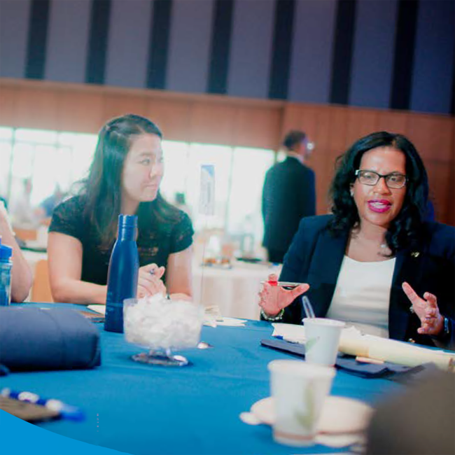 General Manager Kishia L. Powell speaking at a table of Tap Into Business attendees. 